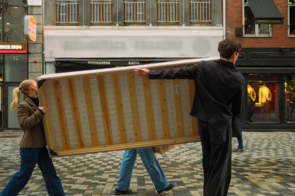 Zwei Helfer tragen ein Sofa über einen gepflasterten Platz