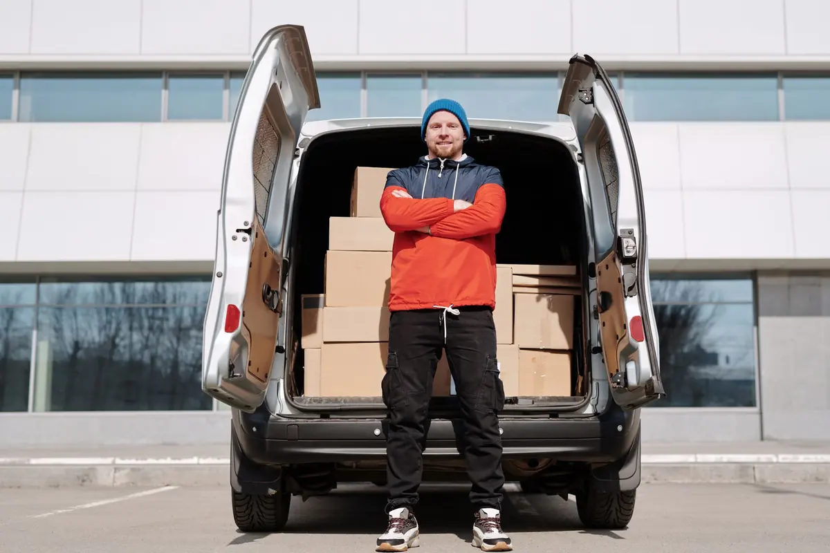 Ein Helfer steht mit einem Karton im offenen Transporter